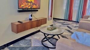 Una sala de estar con un televisor montado en la pared, una mesa de centro, un sofá, un mueble y un suelo estampado.