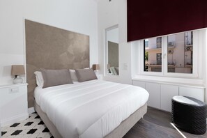 A modern bedroom with a large bed, a window with a view, a mirror, and a nightstand with a lamp. - AMORE RENTALS - Diamond Home De Luxe - Luxury Apartment with Terrace in Central Sorrento (Sorrento)