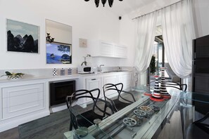 A modern kitchen with white cabinetry, a glass dining table, and decorative items. - AMORE RENTALS - Diamond Home De Luxe - Luxury Apartment with Terrace in Central Sorrento (Sorrento)