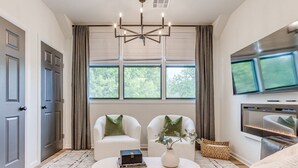 Un salón con chimenea, dos sillones blancos, una mesa de centro con libros y un jarrón, y un televisor de pantalla plana sobre la chimenea.