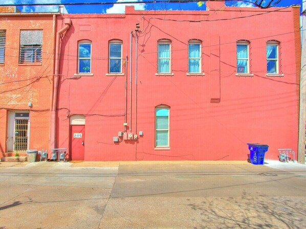 Un bâtiment rouge avec de nombreuses fenêtres, une porte et une poubelle bleue sur le trottoir.