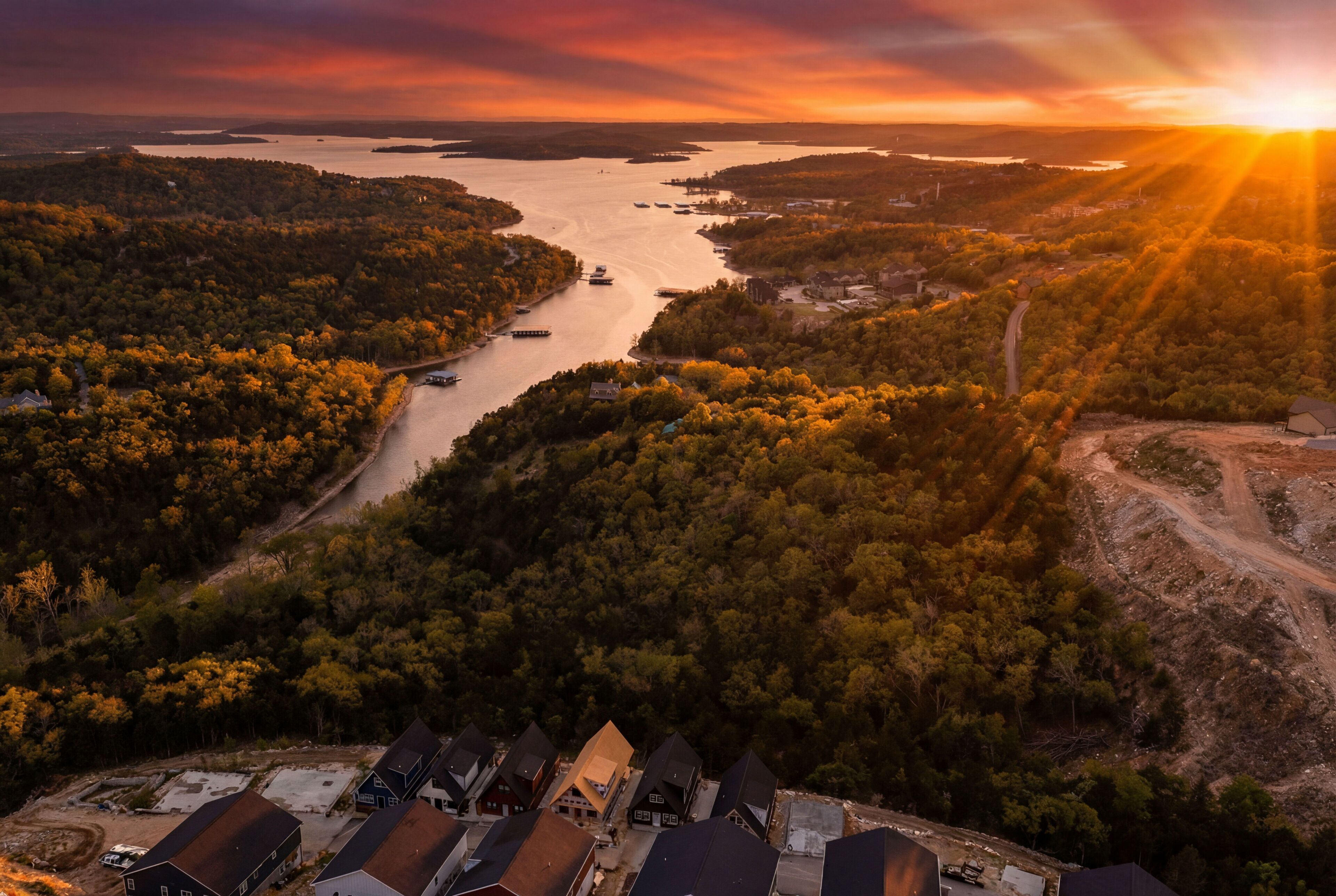 An aerial view of a forested area with a river, boats, and houses with steep roofs.