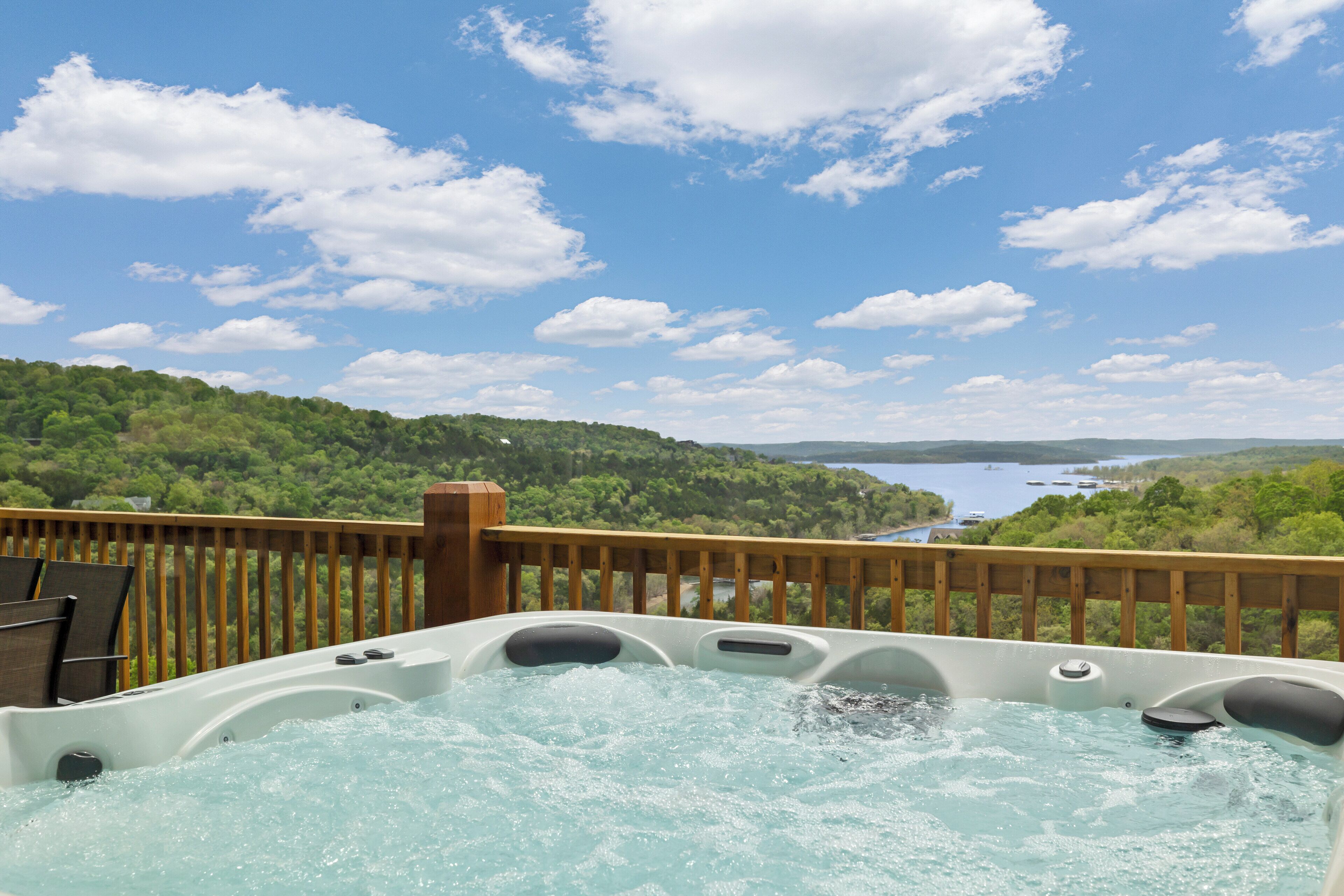 A hot tub with a wooden deck and a scenic view of a lake and forest.