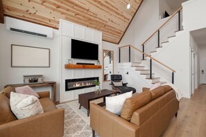 A modern living room with a fireplace, leather sofas, a TV, and a staircase. - Modern A-Frame + Hot Tub with Lake Views Near Branson (MARVEL CAV PK)