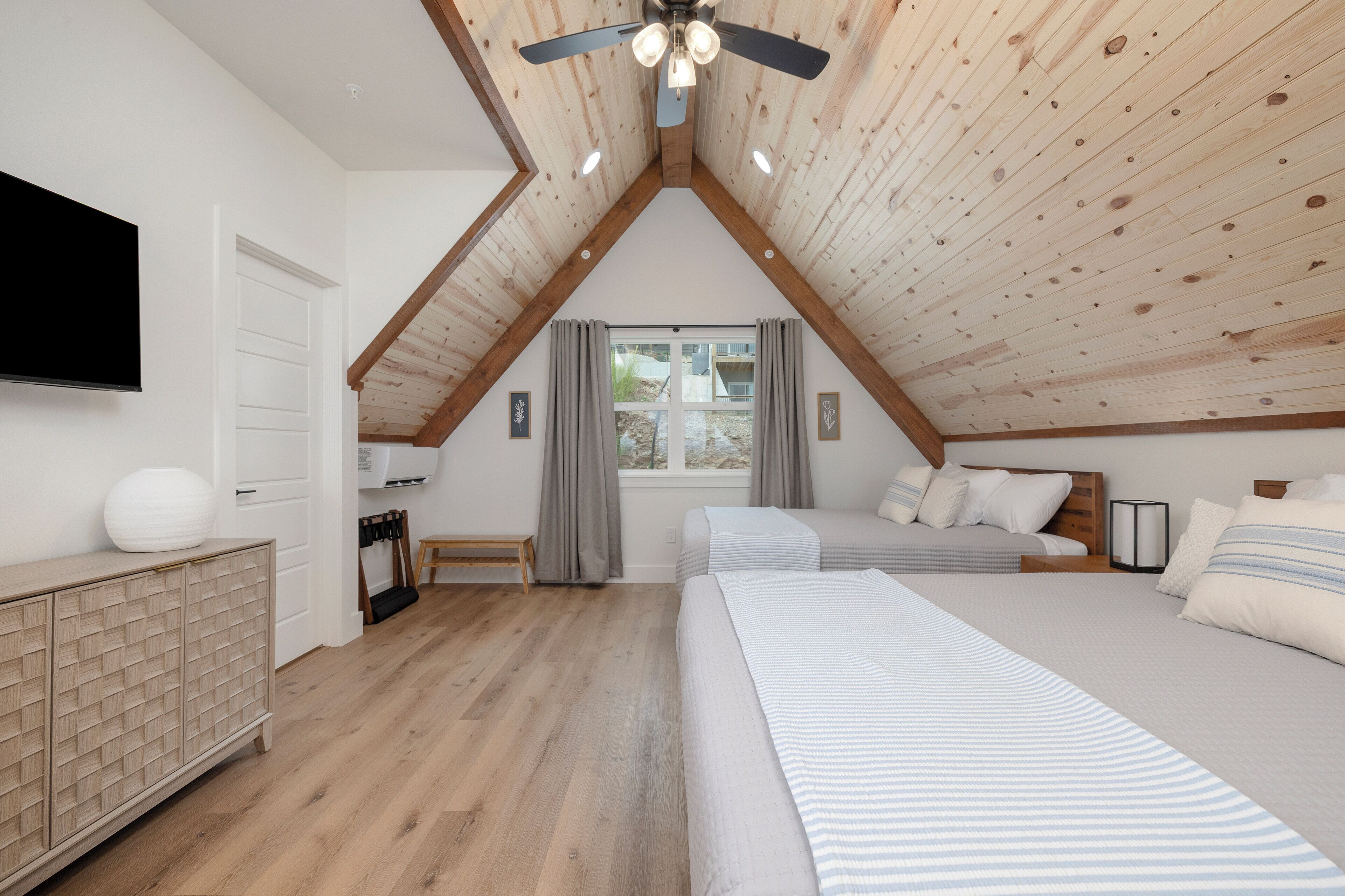 A bedroom with a sloped ceiling, a bed, a bedside table, a TV, and a window with curtains.