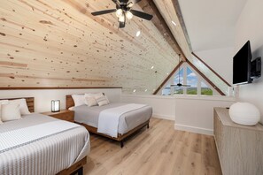 A bedroom with two beds, a ceiling fan, a TV, and a large window with a view. - Modern A-Frame + Hot Tub with Lake Views Near Branson (MARVEL CAV PK)