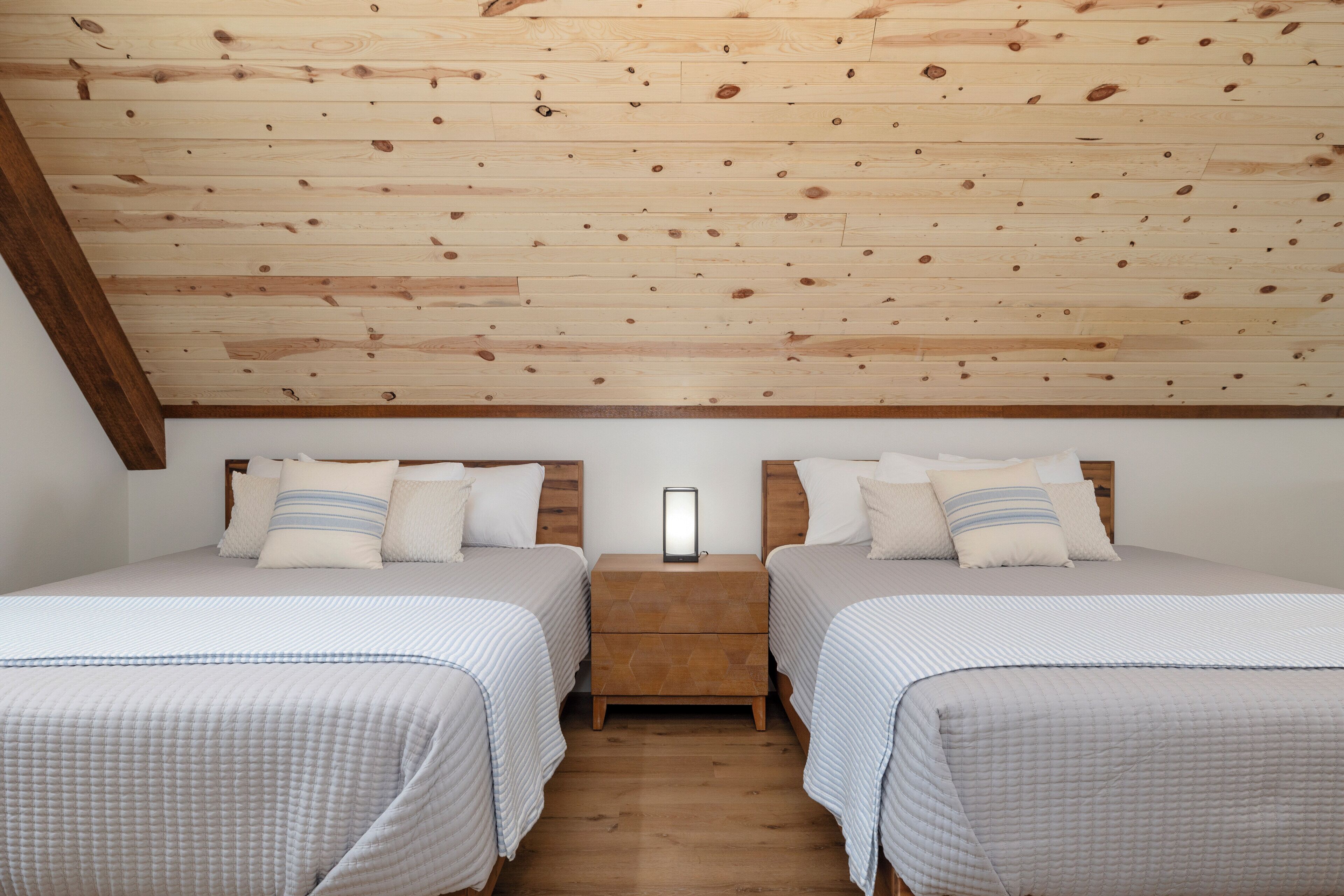 A bedroom with two beds, wooden ceiling, and a nightstand with a mirror.