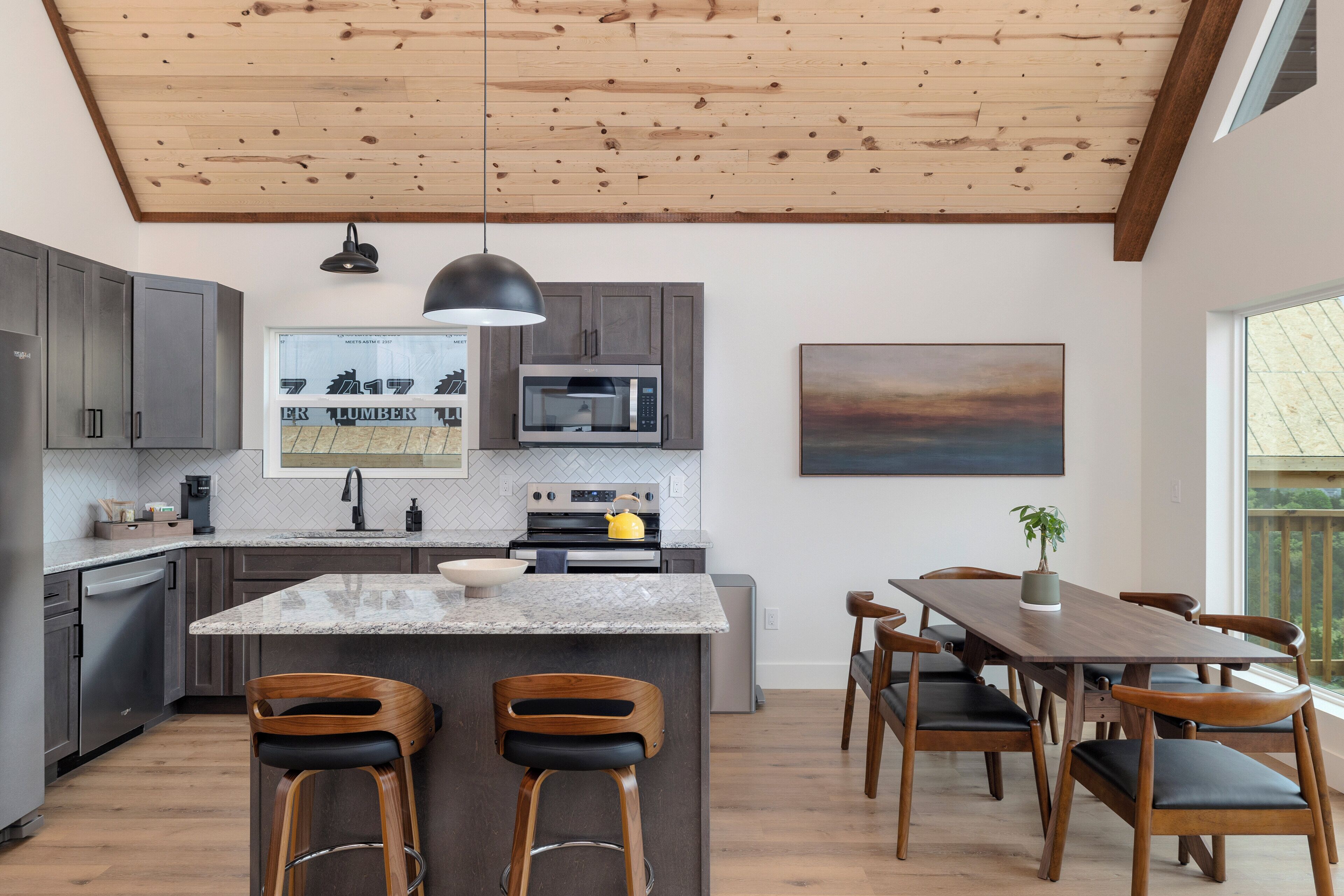 A modern kitchen with a wooden ceiling, granite countertops, and a central island with bar stools.