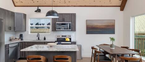 A modern kitchen with a wooden ceiling, granite countertops, and a central island with bar stools.
