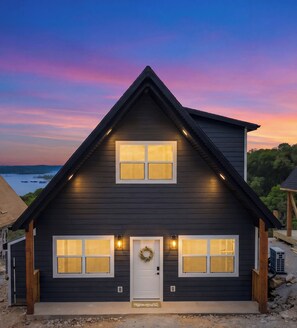 A two-story house with a dark exterior, a front door with a wreath, and two windows on each floor. - Modern A-Frame + Hot Tub with Lake Views Near Branson (MARVEL CAV PK)