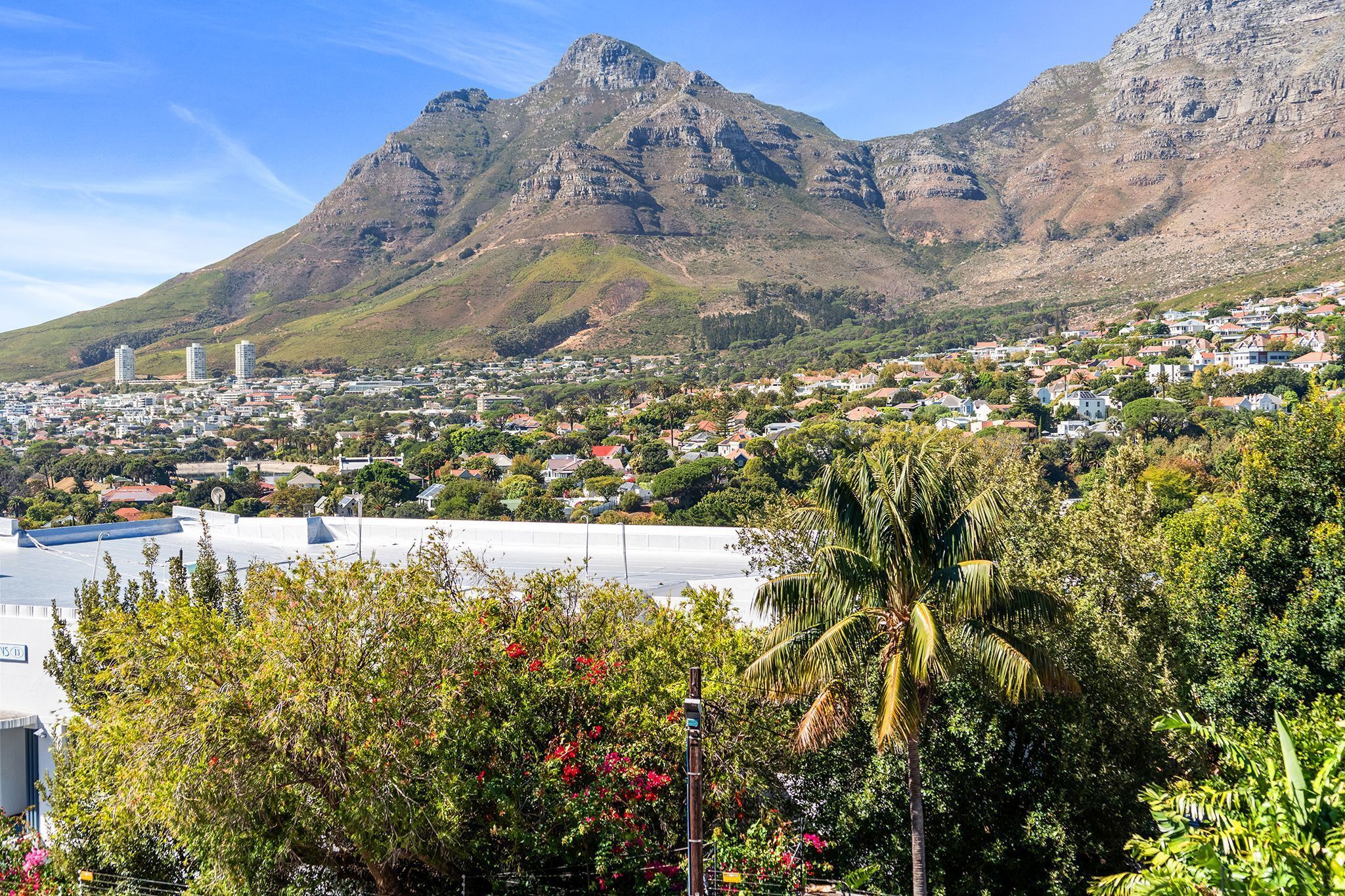 A town with a prominent mountain in the background, residential buildings, and lush greenery.