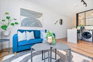 A modern living room with a blue sofa, a coffee table, a potted plant, and a large abstract painting on the wall. - The Cedar 202 (Cape Town)
