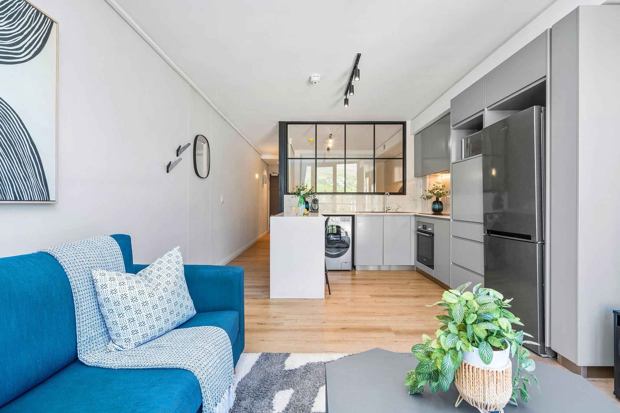 A modern kitchen with a built-in refrigerator, a dining area with a white island, and a blue sofa with patterned cushions.