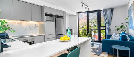 A modern kitchen with a marble backsplash, a dining area with a white table, and a blue sofa in a living space with a view.