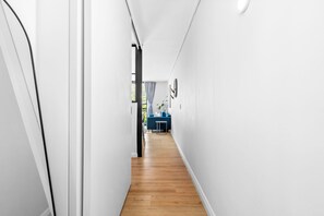 A narrow hallway with wooden flooring, white walls, and a blue sofa in the distance. - The Cedar 202 (Cape Town)