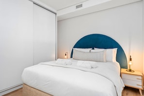 A modern bedroom with a large bed, a nightstand with a lamp, and a wall-mounted light. - The Cedar 202 (Cape Town)