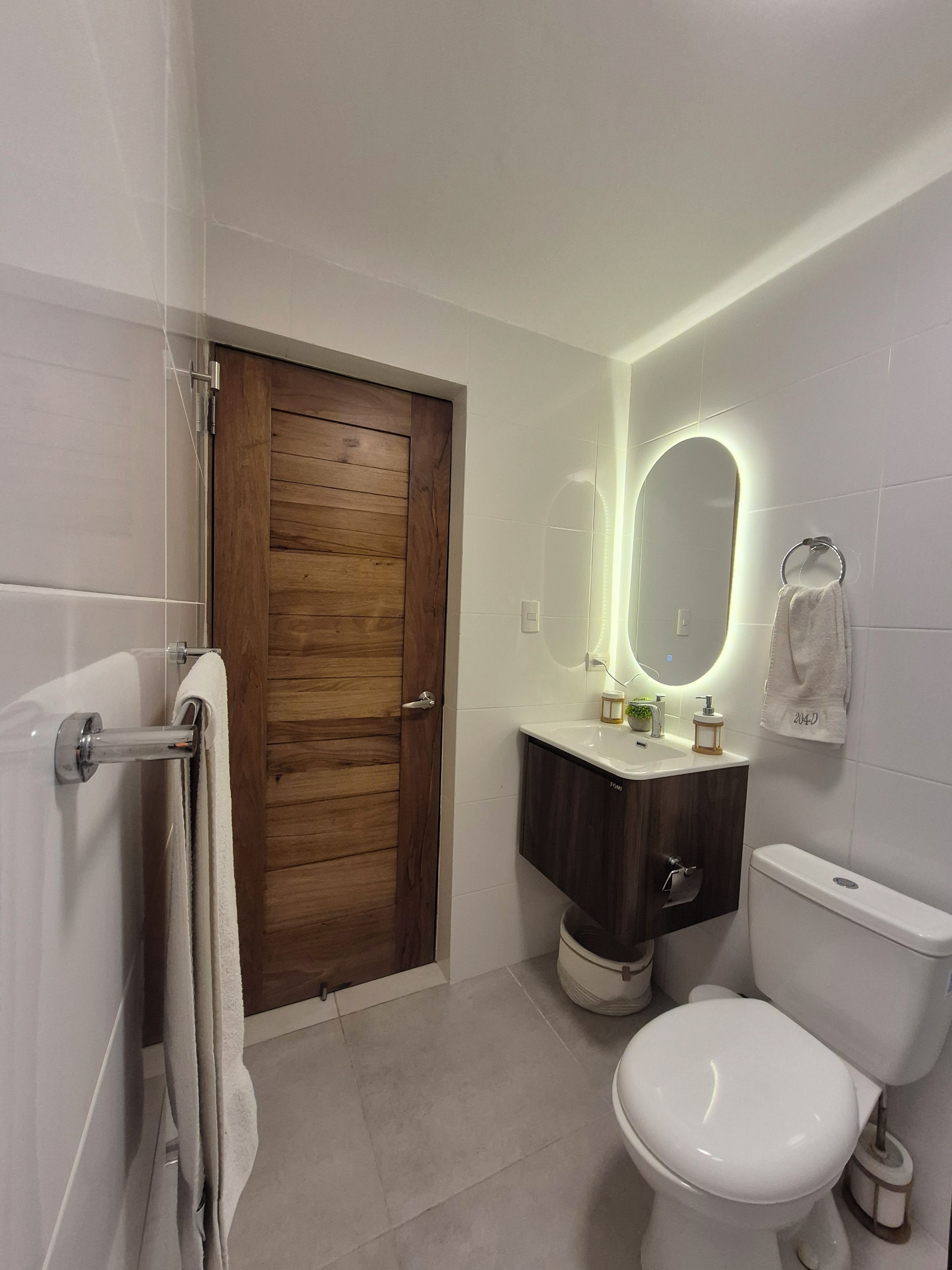 A modern bathroom with a wooden door, a white toilet, a vanity with a mirror, and a towel rack.