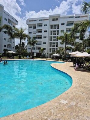 Ein Pool mit geschwungener Kante, umgeben von Palmen und Liegestühlen.