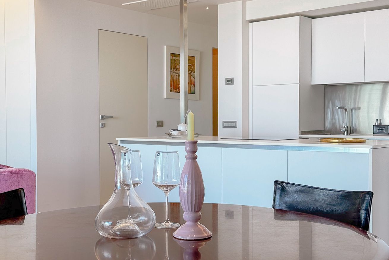 A modern kitchen with white cabinets, a dining table with a vase and wine glasses, and a black leather chair.