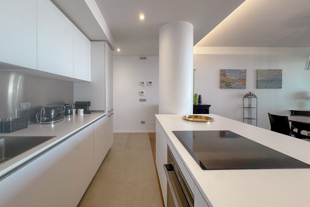 Een moderne keuken met witte kasten, een centraal eiland en een eethoek met een tafel en stoelen.