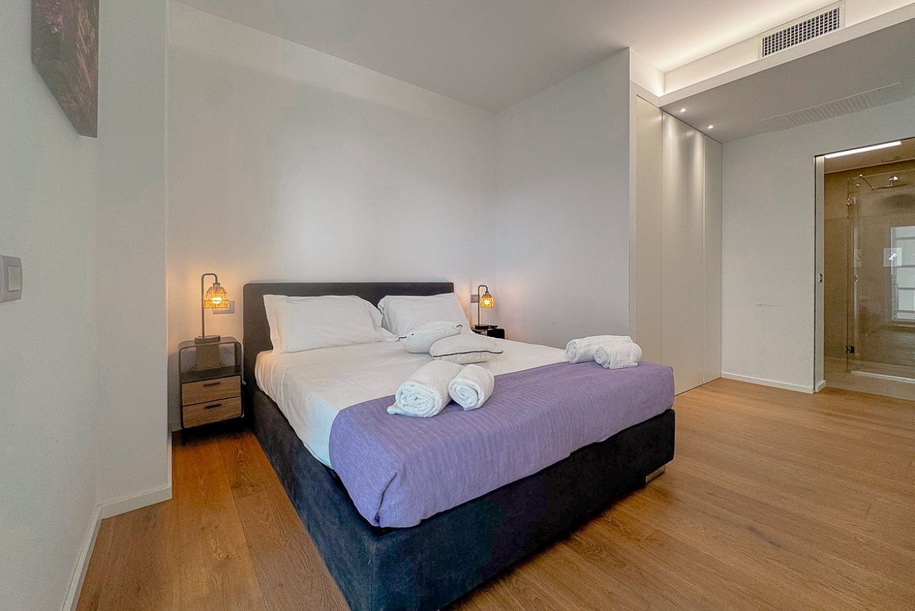 A modern hotel room with a large bed, bedside lamps, and a wooden floor.