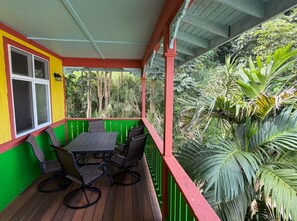A covered outdoor area with a table and chairs, surrounded by greenery. - Serene 2-bedroom apartment in charming Kapaau perfect for relaxing stay (Kapaau)