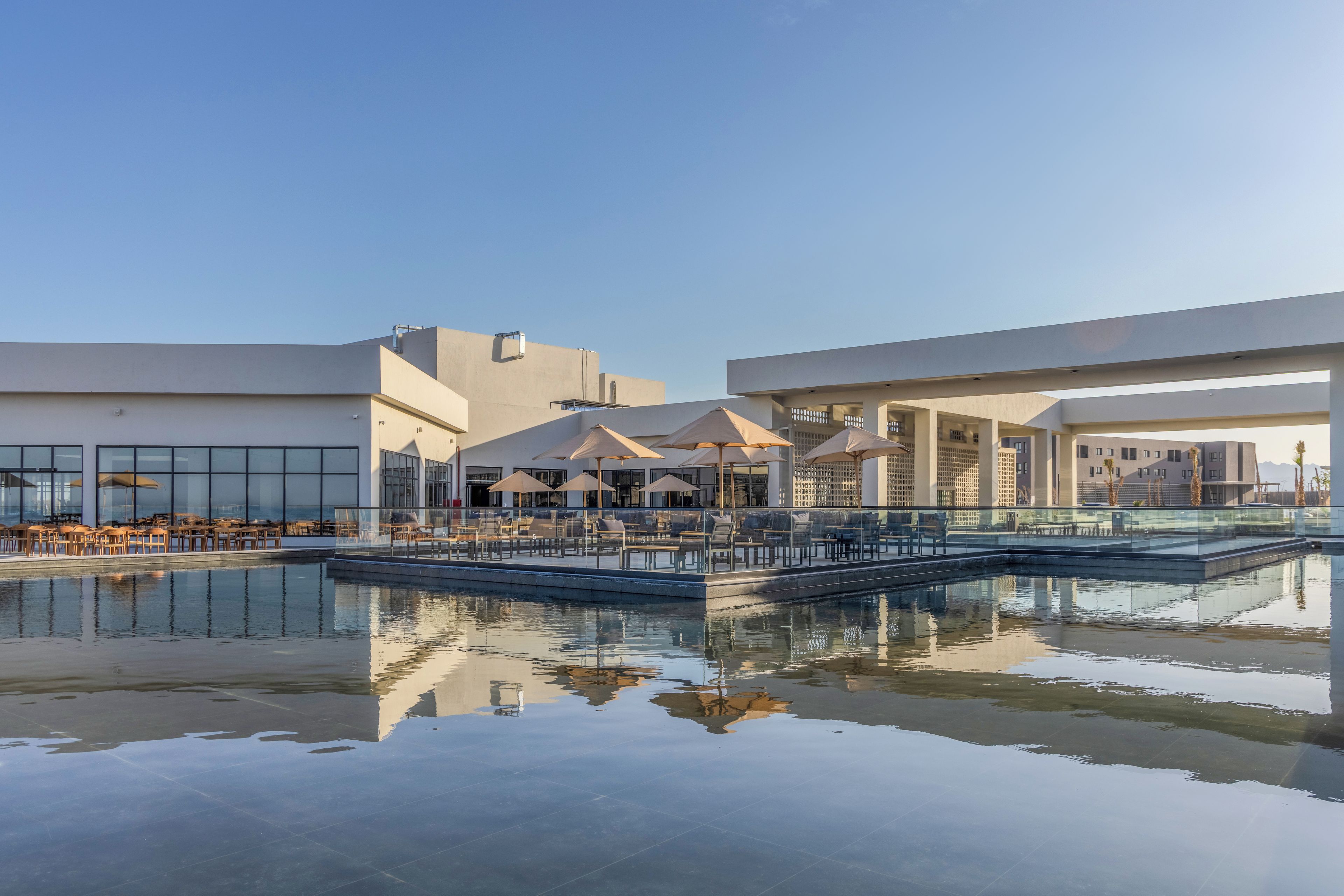 Un espace piscine extérieur moderne, doté de chaises longues et de parasols, et entouré de bâtiments contemporains.