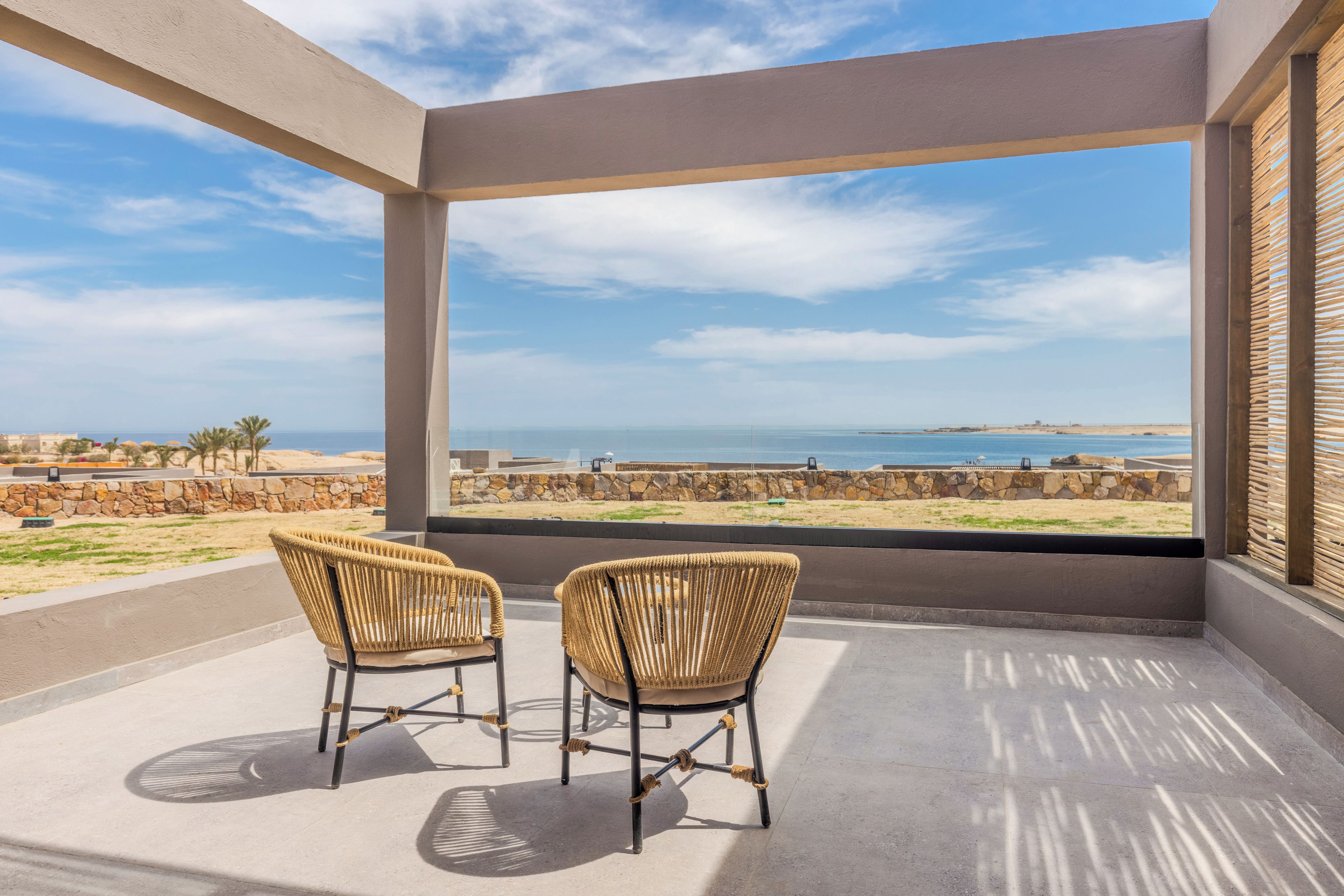 A balcony with two wicker chairs facing a coastal view.