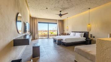 Habitación de hotel con cama, escritorio, silla, balcón con mobiliario exterior y ventilador de techo.