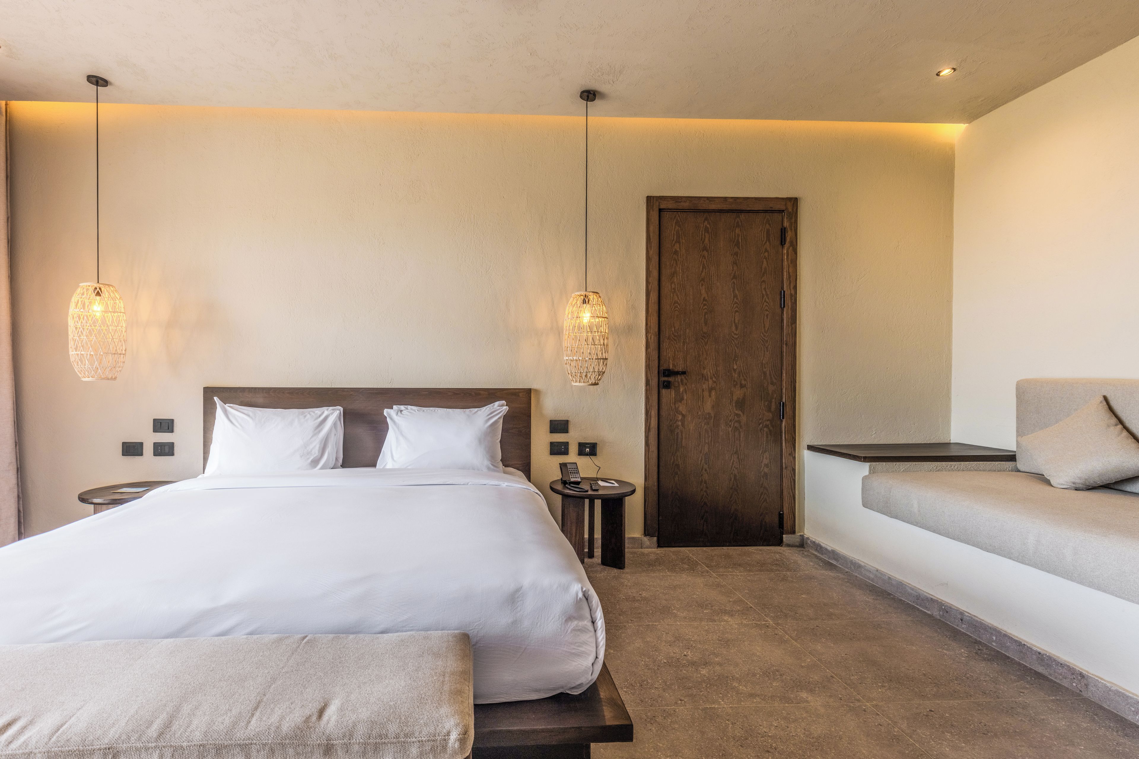 A hotel room with a large bed, bedside tables, a sofa, and two pendant lights.