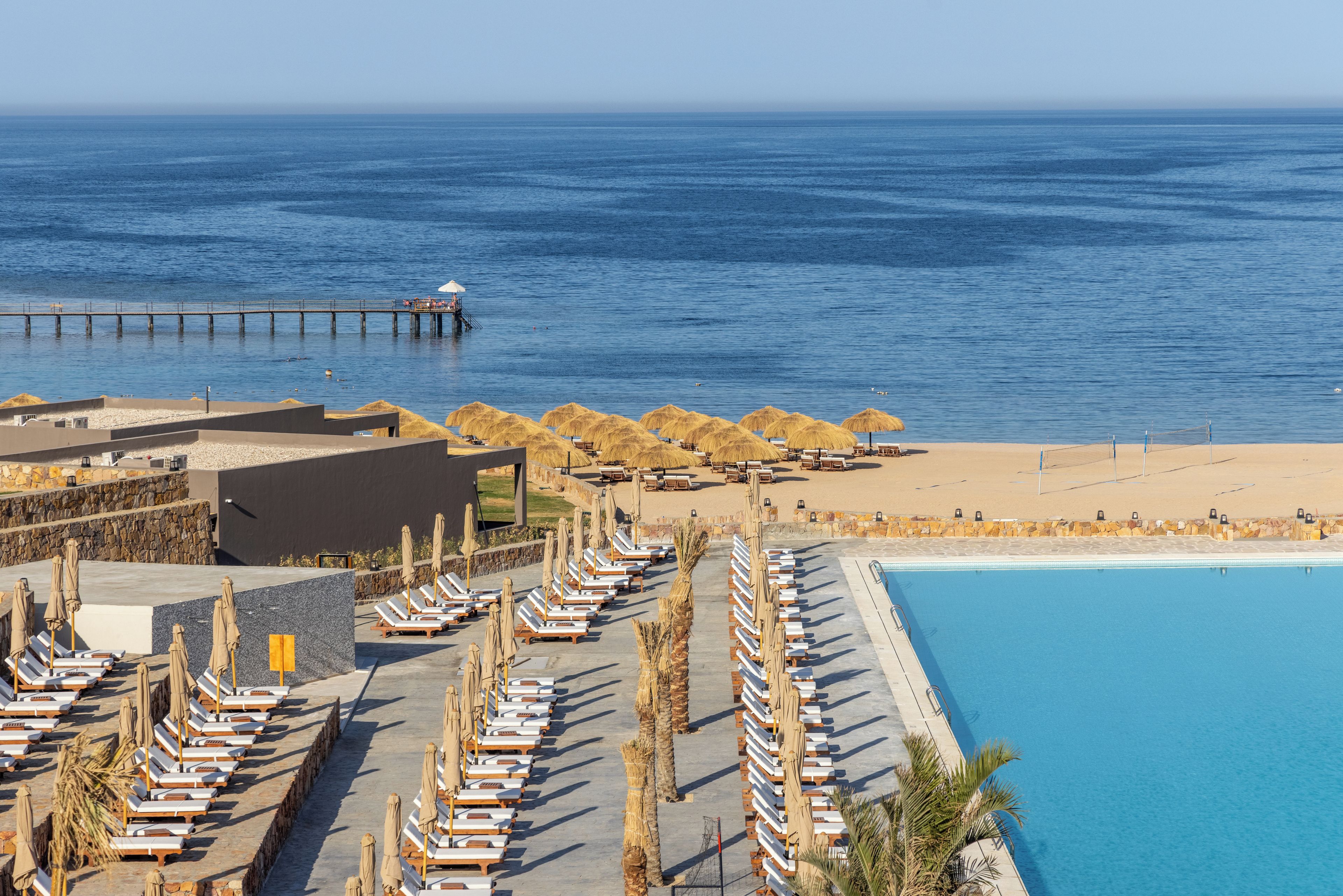 Un resort con piscina, tumbonas y un muelle que se adentra en el mar.