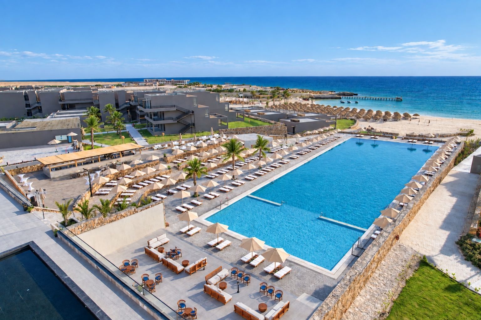 A resort with a large pool, sun loungers, and a beach view.