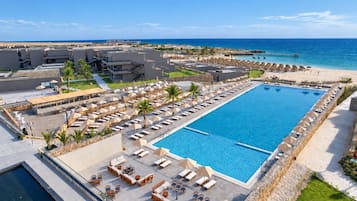 A resort with a large pool, sun loungers, and a beach view.