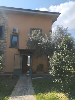 A two-story building with a stone facade, a flat roof, and a small garden area with a pathway leading to the entrance.