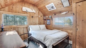 Une chambre confortable dans un chalet, avec un lit, un bureau en bois et une fenêtre donnant sur une forêt.