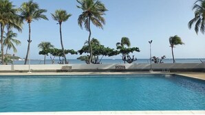 A swimming pool with palm trees and a view of the ocean. - Charming beachfront retreat (Porlamar)
