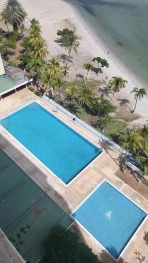 A swimming pool adjacent to a beach with palm trees. - Charming beachfront retreat (Porlamar)