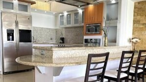 A modern kitchen with a central island, bar stools, stainless steel appliances, and a stone backsplash. - Charming beachfront retreat (Porlamar)