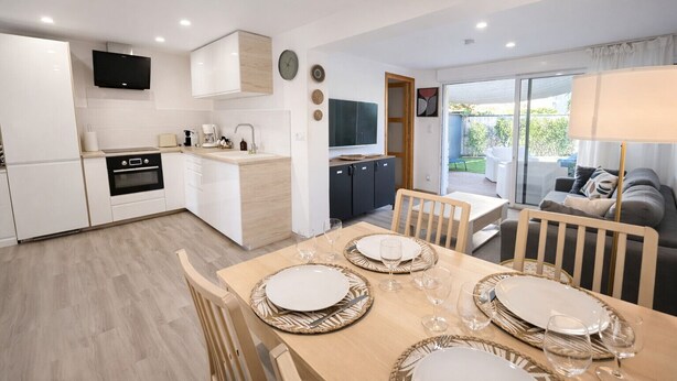 A modern kitchen with a dining area, a TV, and a view of the outdoors. - LVAM - Renovated 2-bedroom apartment – Beach – Garden – Golf 5 (Agde)