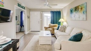 A living room with a white sofa, a coffee table, a TV, and a ceiling fan. - Indoor Outdoor Pools, Balcony and Fenced Yard, Walk to Beach (Ocean City)
