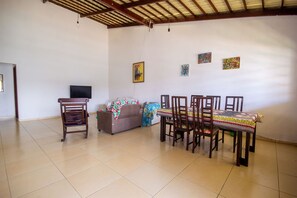 A living room with a sofa, a television, a dining table with chairs, and artwork on the walls. - Casa com Piscina e Ar Perto da Praia em Paripueira (Paripueira)
