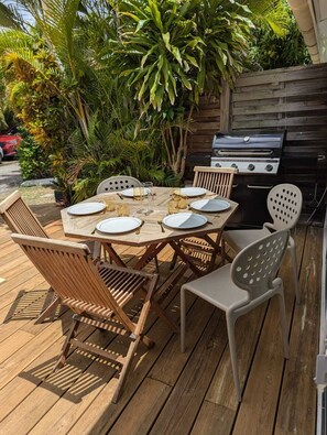 Een buitenterras met een houten tafel, stoelen en een barbecue.
