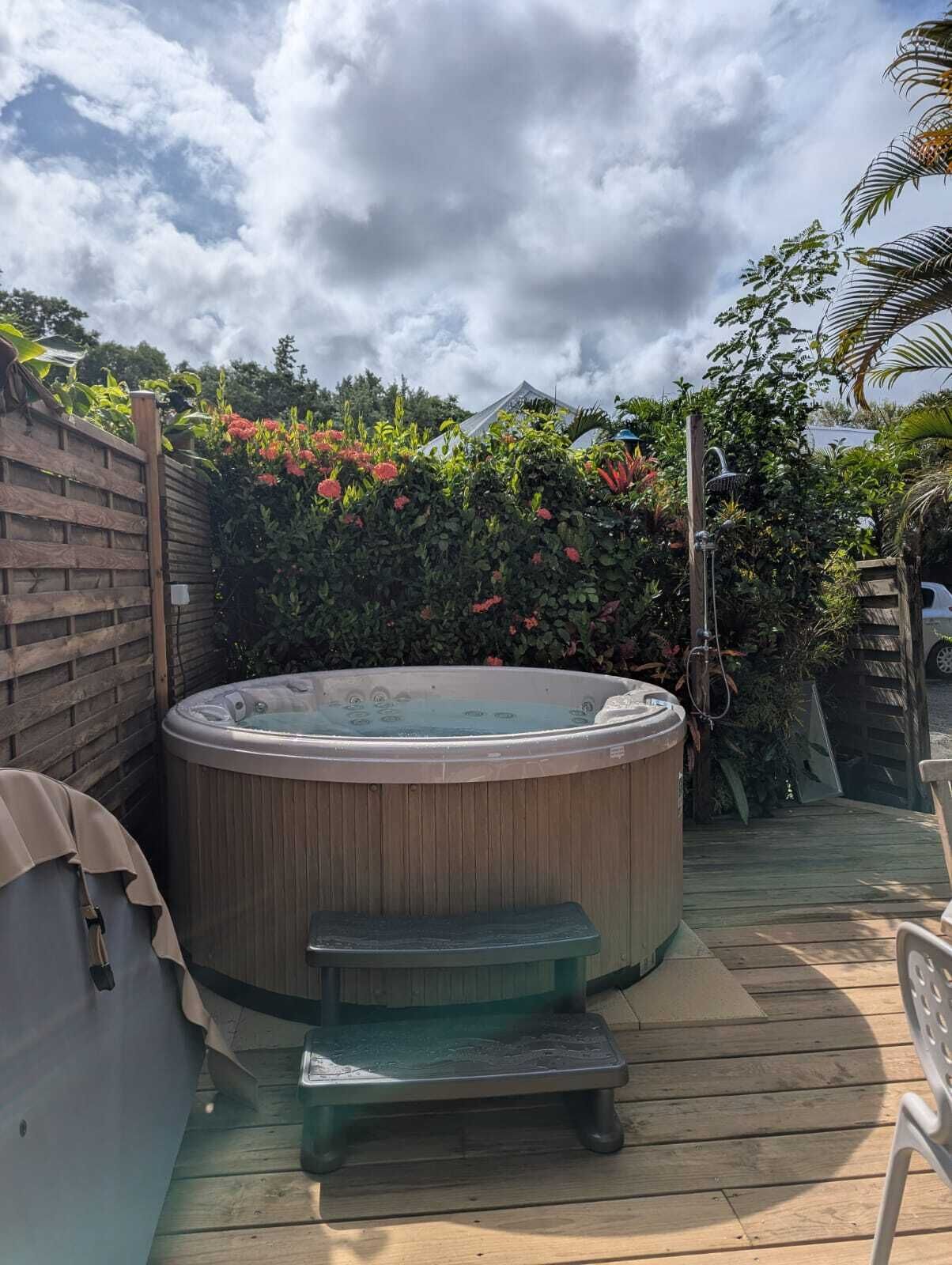A hot tub on a wooden deck with a wooden fence and lush greenery in the background.