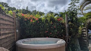 Un jacuzzi en una terraza de madera, con una cerca de madera y abundante vegetación al fondo.