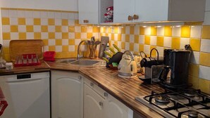 Una cocina compacta con gabinetes blancos, salpicadero a cuadros, estufa y lavavajillas.