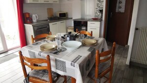 Een eetgedeelte met een tafel voor vier personen, houten stoelen, een keuken op de achtergrond en een rood gordijn aan de linkerkant.