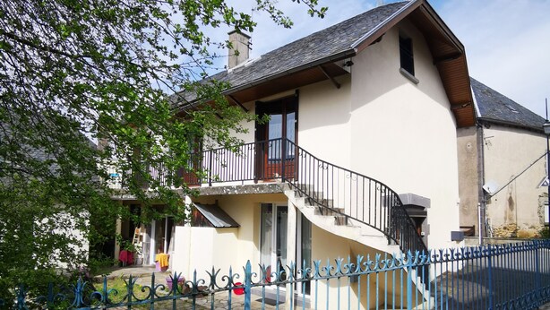 Een twee verdiepingen tellend huis met een balkon, een pad van stenen en een blauwe metalen hek.