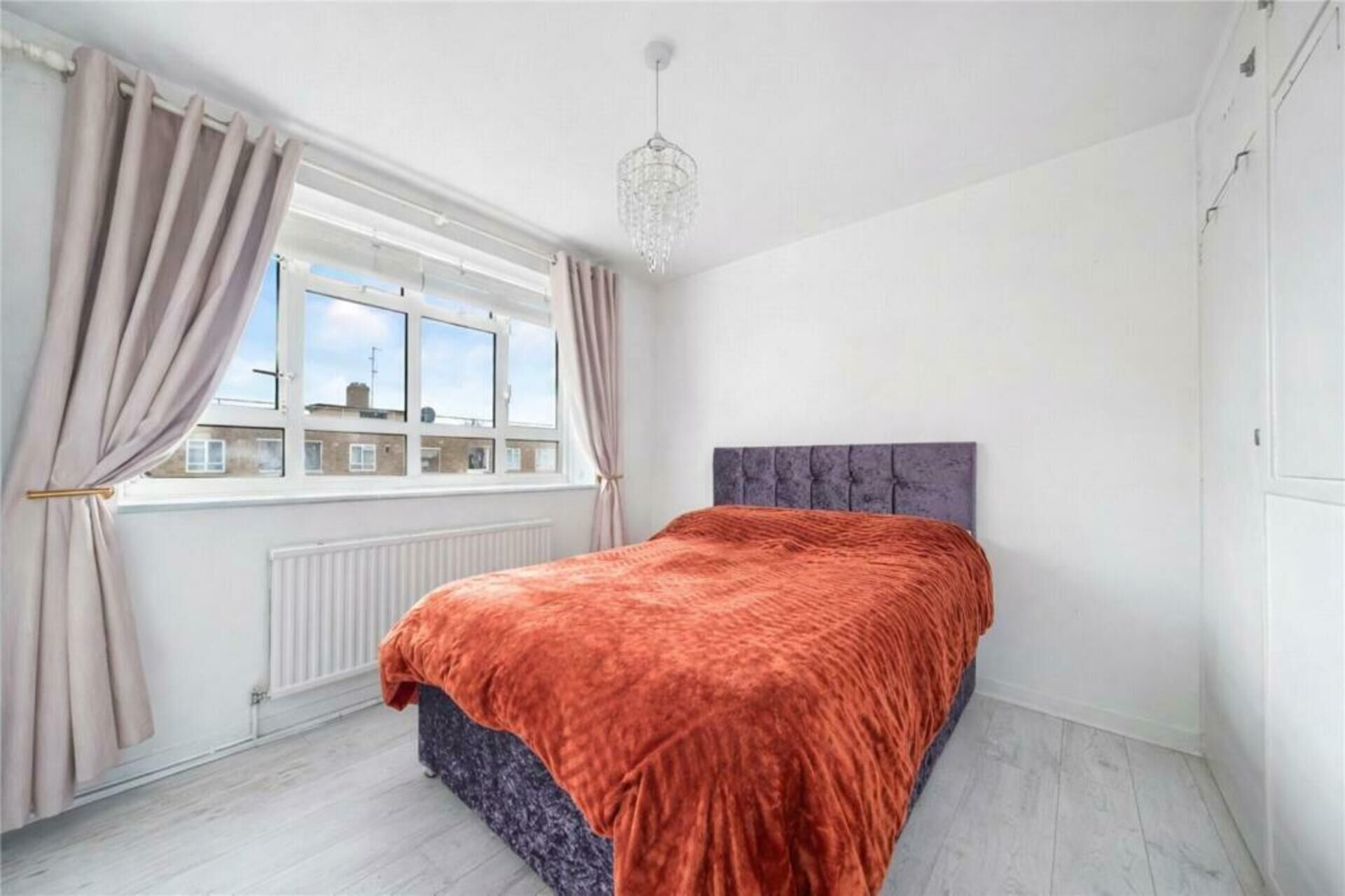 A bedroom with a bed, a window with curtains, a radiator, and a ceiling light fixture.