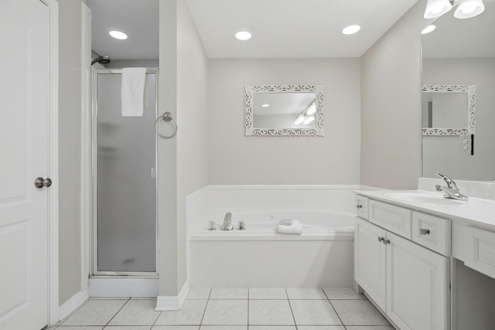 Un baño moderno con ducha, bañera, lavamanos y dos espejos.