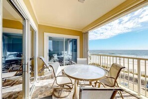 A balcony with a glass door, a round table, and wicker chairs. - Marlin Key 2A (Orange Beach)